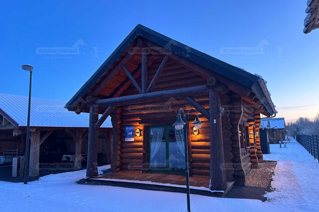 Naturstammhaus Ottawa bei Abenddämmerung im Winter mit massiven Rundholzstämmen und beleuchtetem Eingangsbereich
