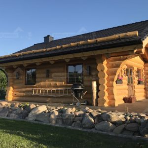 Seitliche Außenansicht des Naturstamm-Gartenhauses Adler mit überdachter Terrasse