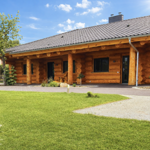 Vorderansicht des Naturstammhauses Bodensee mit überdachtem Eingangsbereich, massiven Rundholzstämmen und breitem Dachüberstand im Gartenbereich