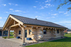 Seitliche Gartenansicht des Naturstammhauses Gransee mit massiven Naturstämmen, Satteldach und umlaufender Holzfassade