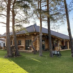 Außenansicht des Naturstammhauses „Potsdam“ mit Rundholzfassade, Satteldach und naturnaher Gartenfläche im Sommer