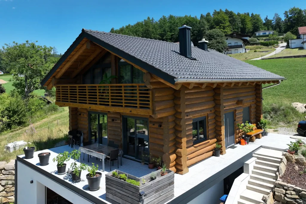 Außenansicht eines Naturstammhauses mit integrierter Garage im Untergeschoss, umlaufender Terrasse und Baukörper in Hangbebauung