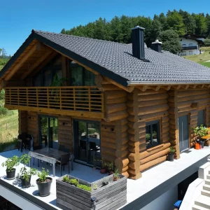 Außenansicht eines Naturstammhauses mit integrierter Garage im Untergeschoss, umlaufender Terrasse und Baukörper in Hangbebauung