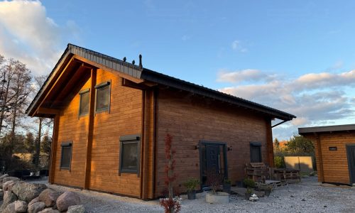 Vorderseite des Blockbohlenhauses Drebkau mit Holzfassade, Satteldach und gepflegter Gartenanlage