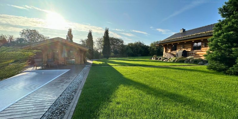 Naturstammblockhaus Sauna aus Rundstämmen im Garten mit sichtbarem Naturstammhaus Adler im Hintergrund